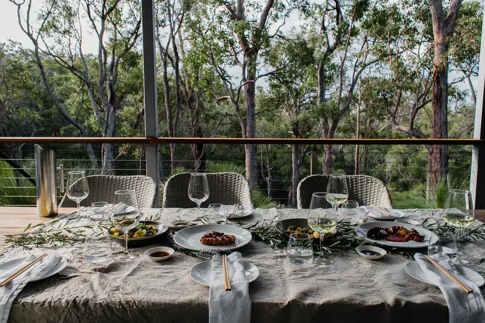 A rustic outdoor dining table set with wild food dishes amidst a tranquil forest setting
